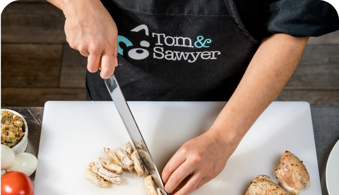 A Tom&Sawyer chef slicing cooked chicken breast on a cutting board